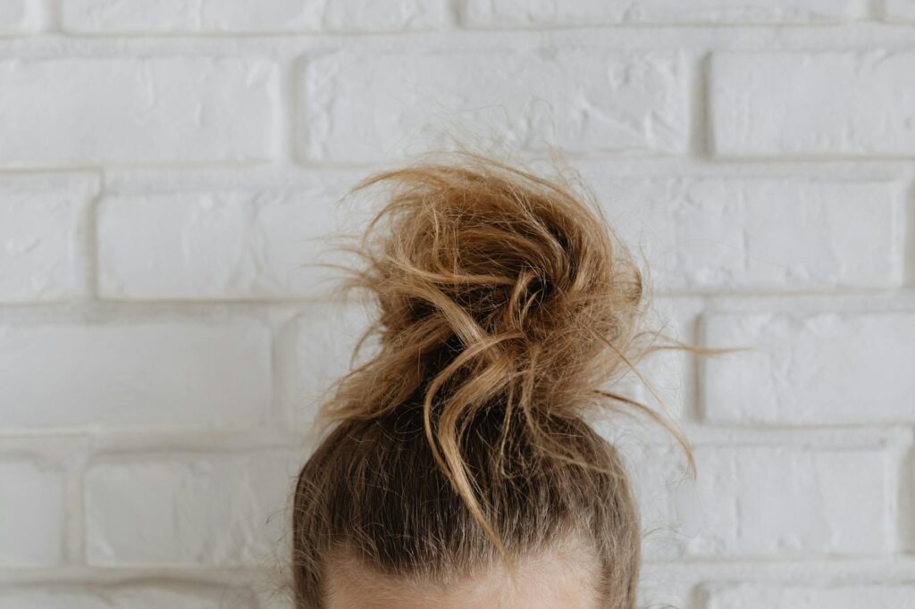 Close-up of a casual messy bun hairstyle in front of a textured white brick wall.